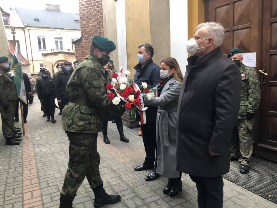 Delegacja powiatu płońskiego wręcza wiązankę kwiatów przedstawicielowi mundurowemu w celu złożenia pod pomnikiem Żołnierzy wyklętych