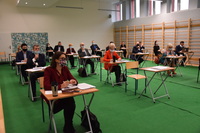 Radni powiatu płońskiego i zaproszeni goście siedzą pojedynczo przy stolikach podczas obrad sesji.jpg