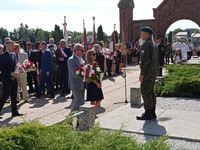 Przedstawiciele powiatu stoją z kwiatami przed pomnikiem żołnierzy bitwy warszawskiej w tle inni uczestnicy uroczystości