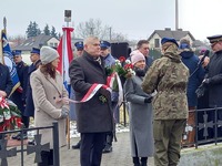 Delegacja powiatu płońskiego przekazuje kwiaty do złożenia pod pomnik pomordowanych