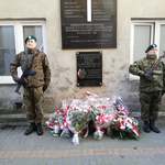 Dwuosobowa warta stoi pod tablicą upamiętniającą Żołnierzy Wyklętych, pod tablicą leżą wiązanki kwiatów